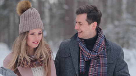 Young-married-couple-in-love-walking-in-the-winter-forest.-A-man-and-a-woman-look-at-each-other-laughing-and-smiling-in-slow-motion.-Valentine's-Day-love-story.